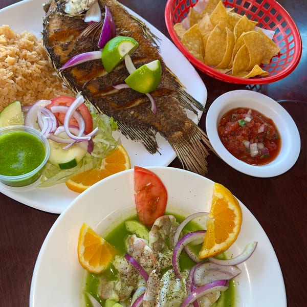 Mexican fried fish with rice, salad, ceviche, chips, and salsa on a wooden table.