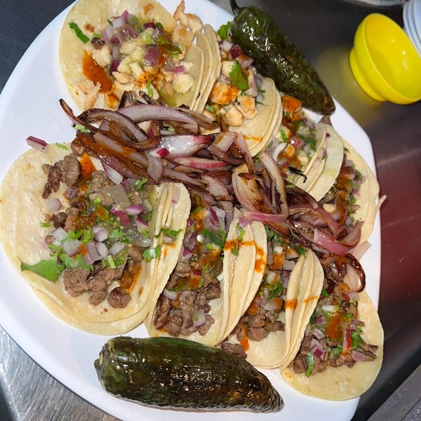 A white plate filled with various Las Brasas Mexican street tacos, garnished with grilled onions and peppers.