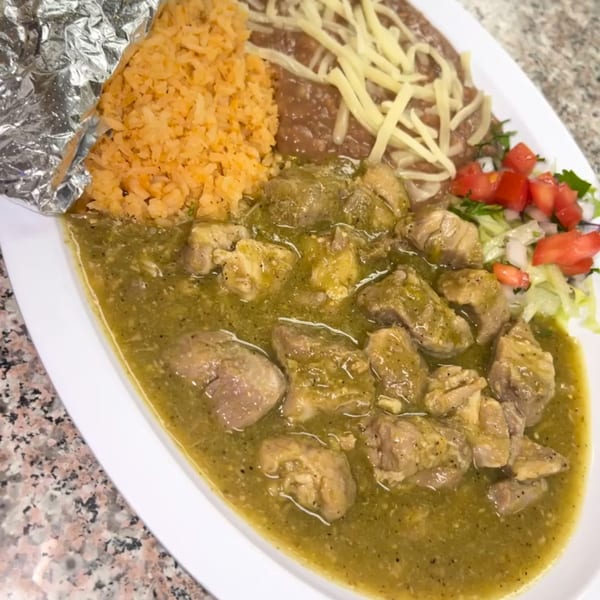 Pork chile verde with rice, refried beans with cheese, and a side salad on a white plate.