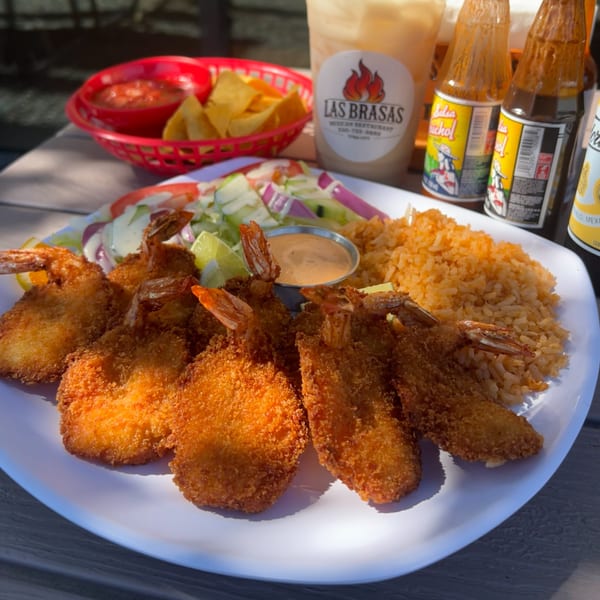 A plate of golden fried shrimp, Mexican rice, salad, and dipping sauce, with chips and salsa in the background.