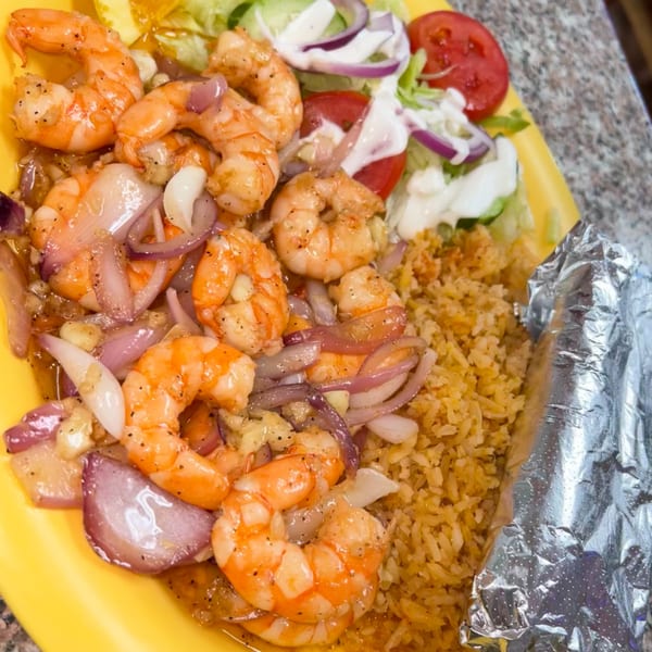 Mexican shrimp dish with sautéed onions, rice, and a side salad with tomatoes and dressing.