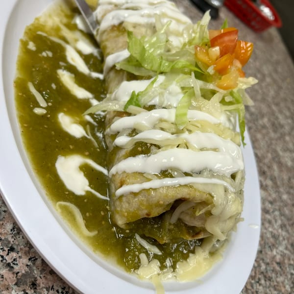A large burrito covered in green salsa, sour cream, shredded lettuce, and diced tomatoes.