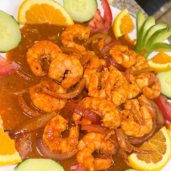 Mexican shrimp dish with red sauce, onions, and garnished with orange slices, cucumbers, and avocado.